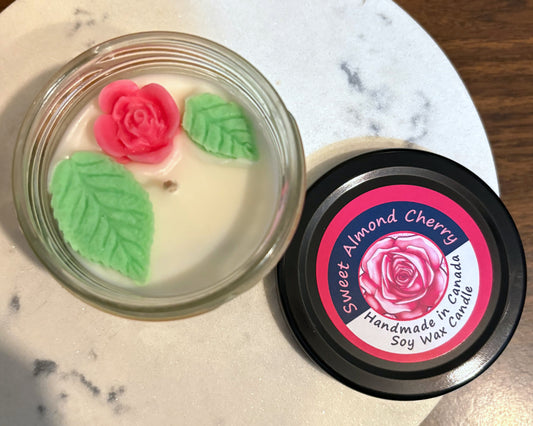 Soy wax candle with rose decorations on a marble surface, featuring 'Sweet Almond Cherry' branding.