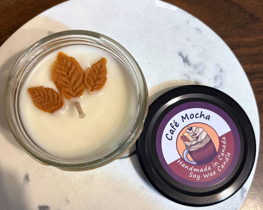 Candle with leaf decorations in a glass jar on a marble surface, featuring 'Cafe Mocha' branding.