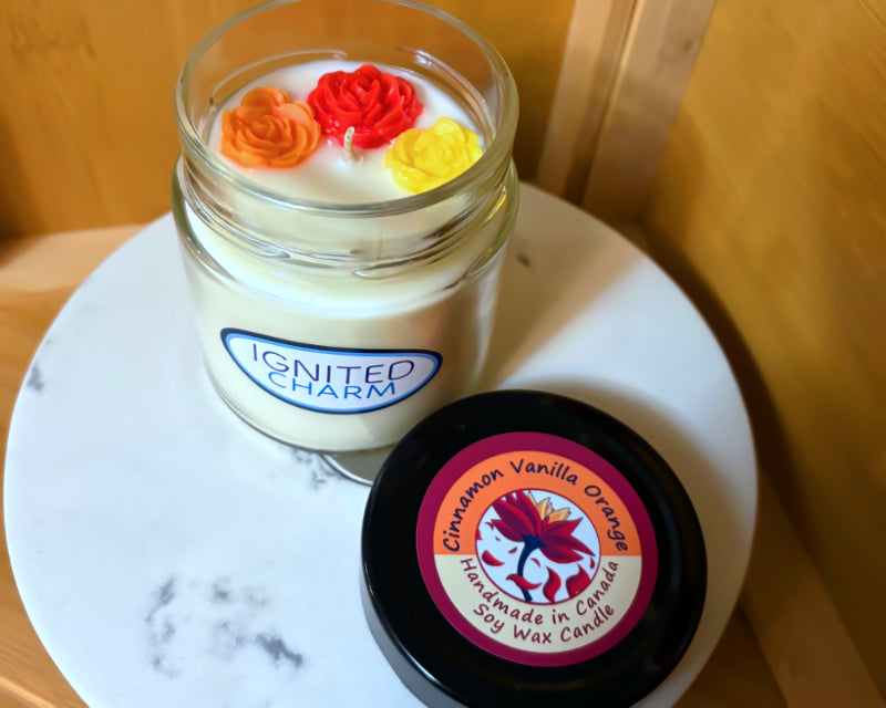 Candle in a glass jar with decorative flowers on top, next to a container labeled 'Ignited Charm' on a marble surface.