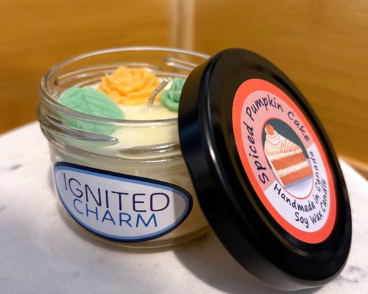 Colourful candle with Ignited Charm sticker and a decorative lid that says Spiced Pumpkin Cake on a marbled surface.