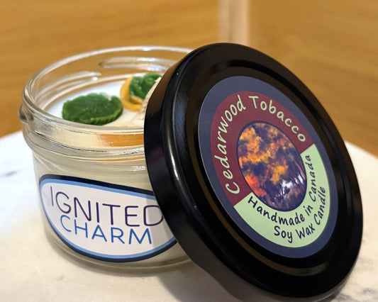 Candle jar with 'Ignited Charm' label and lid with 'Cedarwood Tobacco' label on a marble surface.