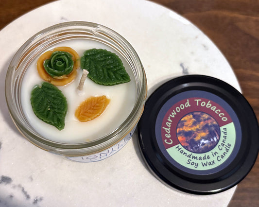 Candle in a glass jar with decorative elements on a white surface, accompanied by a 'Cedarwood Tobacco' candle lid.