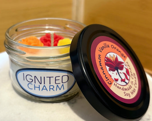 Jar of candles with 'Ignited Charm' label and a candle on a surface with 'Cinnamon Vanilla Orange' label.
