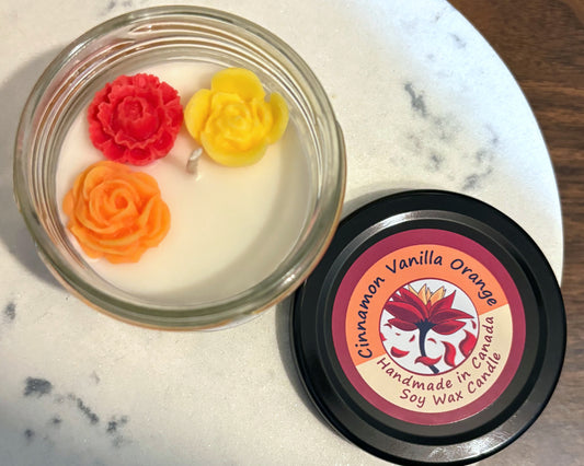 Candle with floral designs on a marble surface, featuring a 'Cinnamon Vanilla Orange' label.